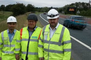 Pictured (left to right) alongside the westbound A66 near Penrith with one of the signs is Highways England project manager Jobert Fermilan, Keith Brown from HW Martin - one of the specialist suppliers supporting the pilot project - and Highways England senior project manager Steve Mason