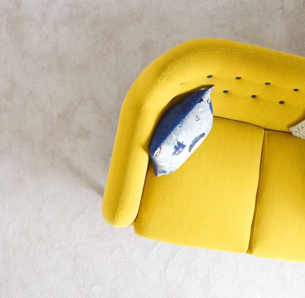 Bird's eye view of a right corner of a yellow sofa with a blue and white pillow on it